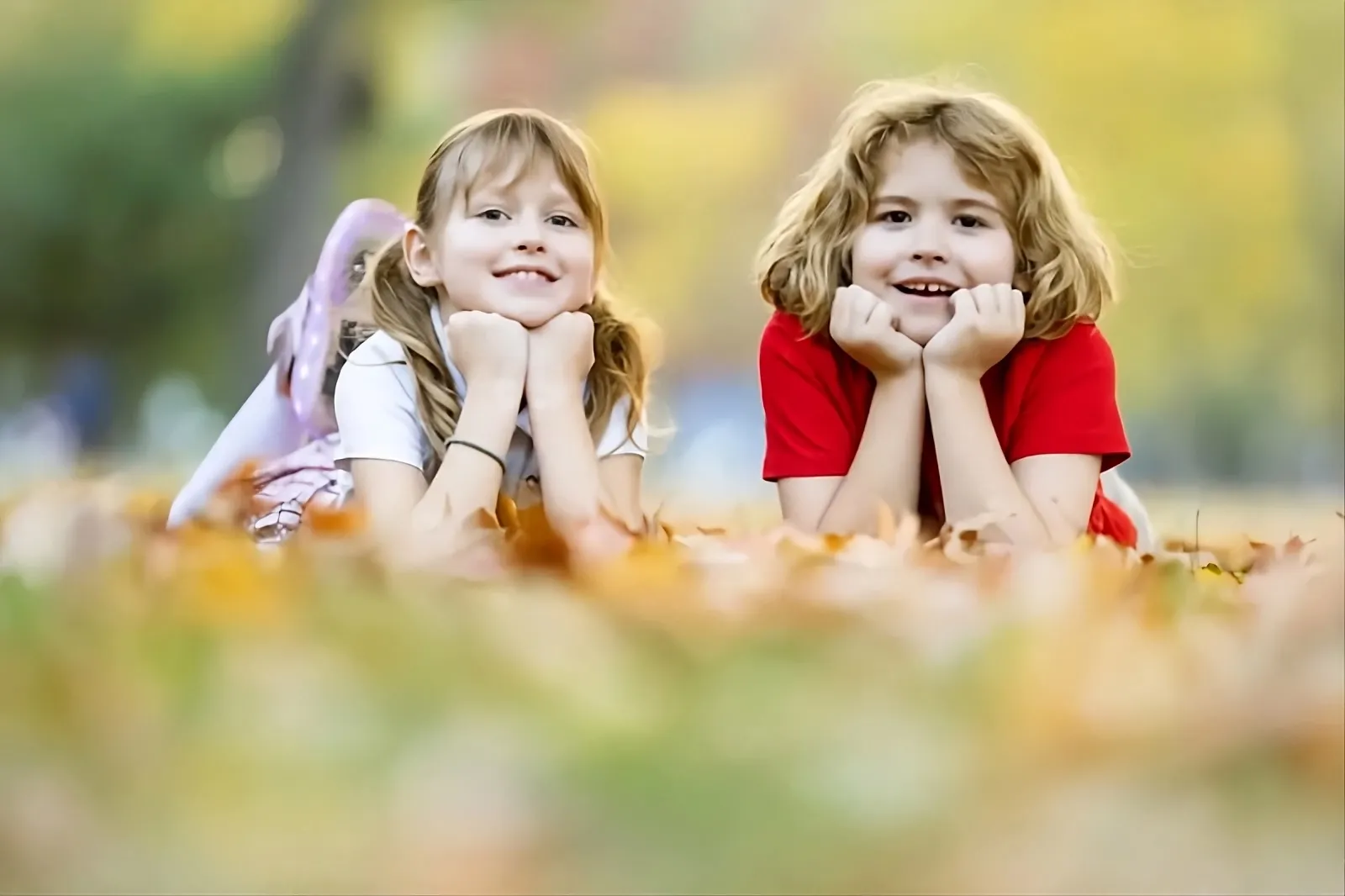 Two smiling children lying in autumn leaves
